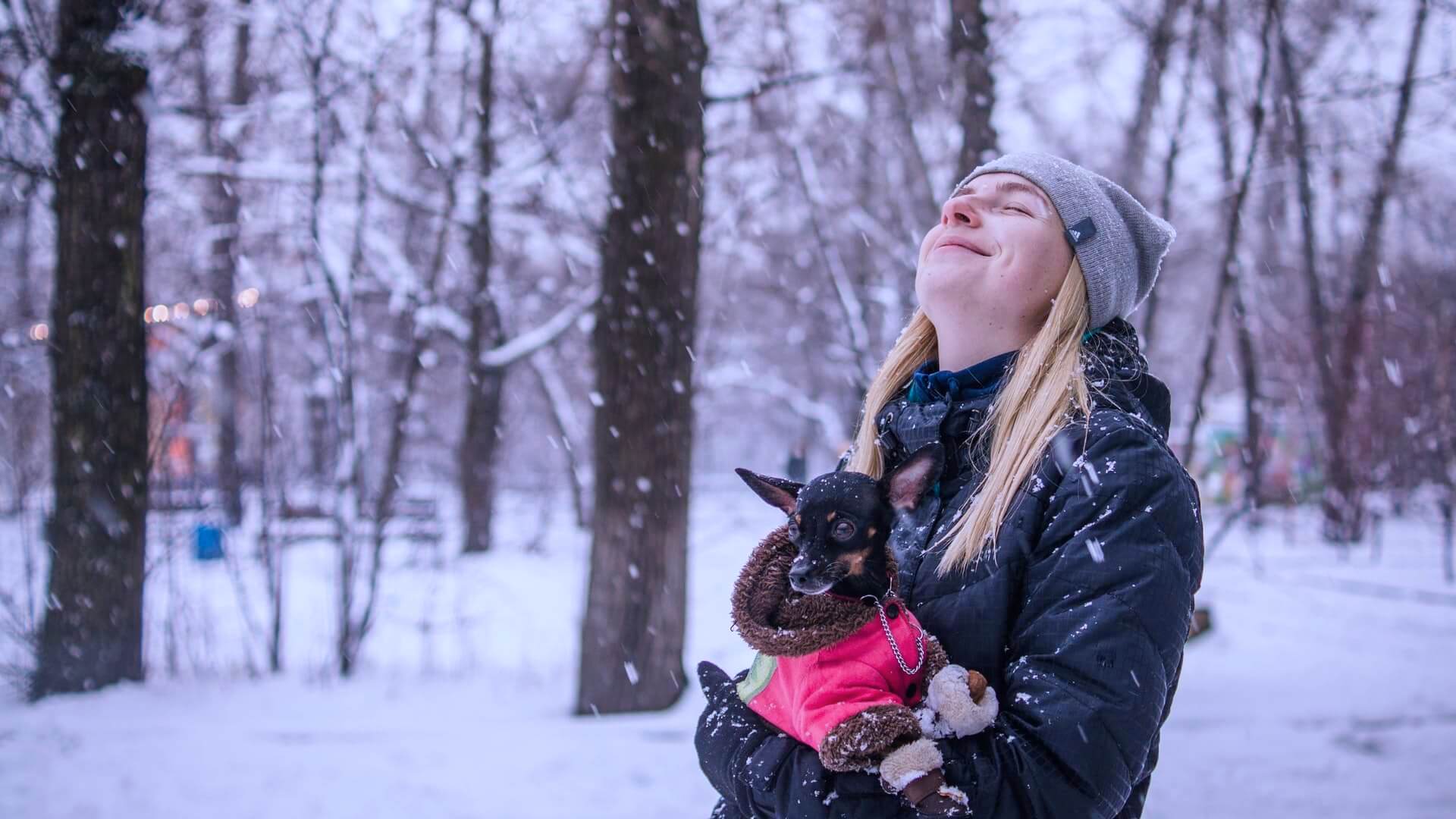 A lady carrying her dog in the snow